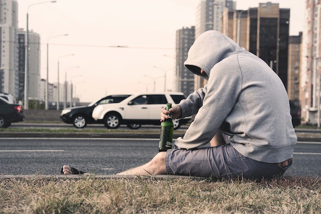 person on side of road with alcohol bottle