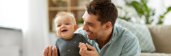 A smiling adult holds a happy baby while sitting on the floor in a bright living room, embracing the joys of co-parenting during the holidays. From Lawrence Law Firm New Jersey Family Lawyer.