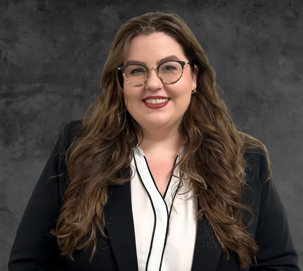 Michelle Thompson, a woman with long brown hair and glasses, wears a black blazer and white blouse while smiling in front of a dark textured background. From Lawrence Law Firm New Jersey Family Lawyer.