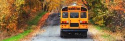 A yellow school bus drives down a rural road surrounded by trees with autumn foliage, while parents use parenting apps for shared custody to stay connected throughout the school day. From Lawrence Law Firm New Jersey Family Lawyer.
