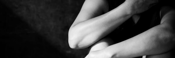 A person sitting with their arms crossed over their knees, partially covering their face, in a dimly lit setting. From Lawrence Law Firm New Jersey Family Lawyer.