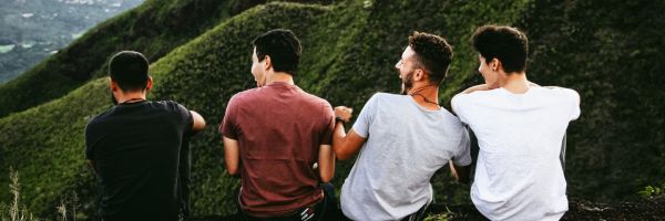 Four people sit in a row outdoors, facing away, with green hills in the background. They appear to be talking and laughing together. From Lawrence Law Firm New Jersey Family Lawyer.