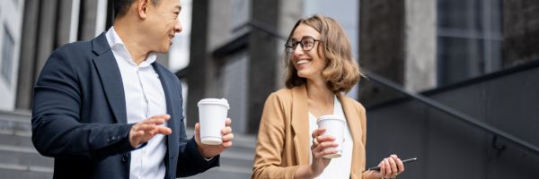 Two people wearing business attire hold coffee cups and walk outside, smiling and talking to each other. From Lawrence Law Firm New Jersey Family Lawyer.