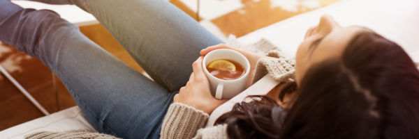 A single parent reclines on a couch, holding a white mug of tea with a lemon slice, savoring a quiet moment during the holiday season, viewed from above. From Lawrence Law Firm New Jersey Family Lawyer.