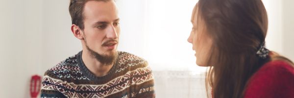 A man and a woman sit indoors facing each other, engaged in a serious conversation about the challenges of being a single parent during the holiday season. From Lawrence Law Firm New Jersey Family Lawyer.