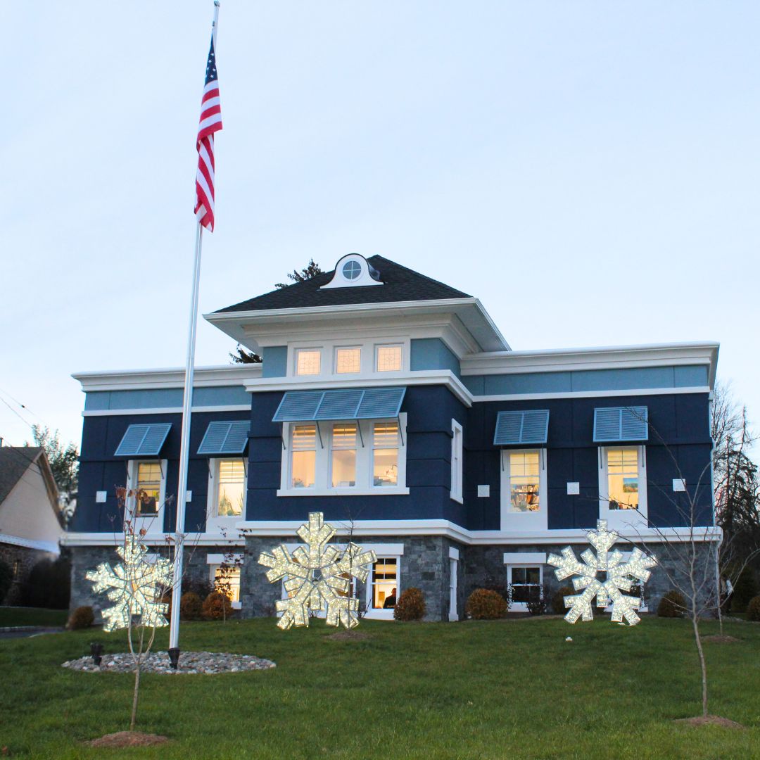 A two-story blue building with large windows, an American flag in front, and three illuminated snowflake decorations on the lawn showcases the welcoming presence of Our Firm. From Lawrence Law Firm New Jersey Family Lawyer.