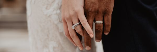 Close-up of two hands with wedding rings, one light-skinned and one dark-skinned, resting side by side against a blurred background—symbolizing unity while reminding couples to consider prenuptial agreements before marriage. From Lawrence Law Firm New Jersey Family Lawyer.