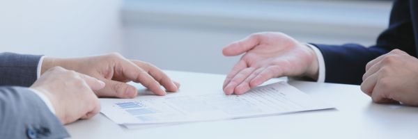 Three people in business attire sit at a table discussing a document with charts and graphs, reviewing important details about prenuptial agreements. From Lawrence Law Firm New Jersey Family Lawyer.