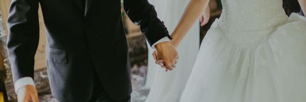 A bride in a white gown and a groom in a black suit hold hands while walking indoors, celebrating their marriage with love and commitment—ready for everything the future brings, including thoughtful discussions about prenuptial agreements. From Lawrence Law Firm New Jersey Family Lawyer.