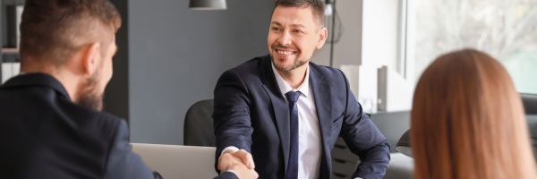 Three people in business attire are seated at a table, with two men shaking hands and a woman sitting across from them, likely discussing a prenuptial agreement before marriage. From Lawrence Law Firm New Jersey Family Lawyer.