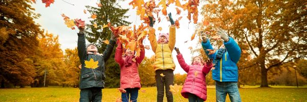 Five children in colorful jackets throw autumn leaves in the air while standing in a park, symbolizing the joy at the heart of Best Interests of the Child considerations in New Jersey custody cases. From Lawrence Law Firm New Jersey Family Lawyer.