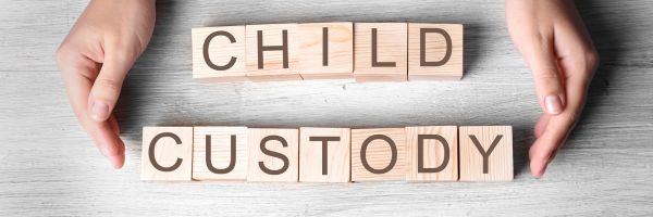 Two hands frame wooden blocks spelling "CHILD CUSTODY" on a light gray wooden surface, representing custody cases and the focus on the best interests of the child in New Jersey custody decisions. From Lawrence Law Firm New Jersey Family Lawyer.