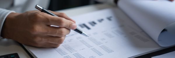 A person holds a pen and reviews a printed financial document with charts and tables on a desk, reflecting on divorce trends that often emerge during January, known as Divorce Month. From Lawrence Law Firm New Jersey Family Lawyer.