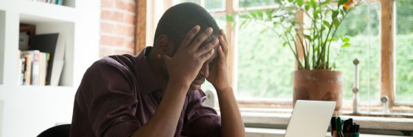 A person sits at a desk with their head in their hands, appearing stressed or frustrated—reflecting January divorce trends—in front of a laptop with a plant and window in the background. From Lawrence Law Firm New Jersey Family Lawyer.