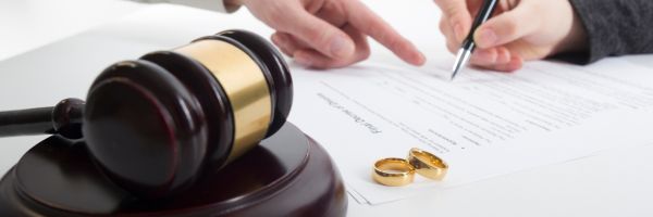 A gavel, two wedding rings, and two people signing a document, highlighting January divorce trends and the legal process often associated with Divorce Month. From Lawrence Law Firm New Jersey Family Lawyer.