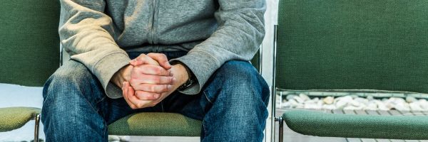 Person sitting on a green chair with hands clasped, wearing a gray hoodie and blue jeans; an empty chair beside them suggests the solitude often felt when you file for divorce in NJ. From Lawrence Law Firm New Jersey Family Lawyer.
