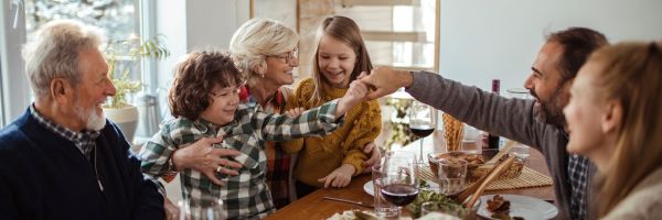 A family of six sits around a dining table, sharing laughter and food in a bright, cozy room—reminding us that even during challenging times like divorce in New Jersey, moments of togetherness still matter. From Lawrence Law Firm New Jersey Family Lawyer.