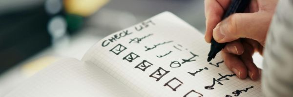 A hand writes on a notebook with a checklist, marking several items with checkmarks and others left unchecked—perhaps setting New Year goals or steps to file for divorce in NJ. From Lawrence Law Firm New Jersey Family Lawyer.