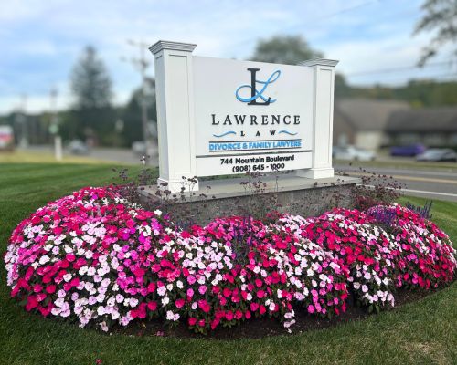 Large outdoor sign for Our Firm, Lawrence Law, Divorce & Family Lawyers, surrounded by pink and white flowers on a grassy area near a street. From Lawrence Law Firm New Jersey Family Lawyer.
