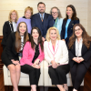 A group of nine professionally dressed people, including Jeralyn Lawrence, comprising eight women and one man, pose together indoors, with some sitting on a couch and others standing behind them. From Lawrence Law Firm New Jersey Family Lawyer.
