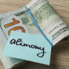 A stack of 100 dollar bills held by a blue rubber band, with a sticky note labeled "alimony" on top—perfect for illustrating financial issues handled by Jeralyn Lawrence. From Lawrence Law Firm New Jersey Family Lawyer.