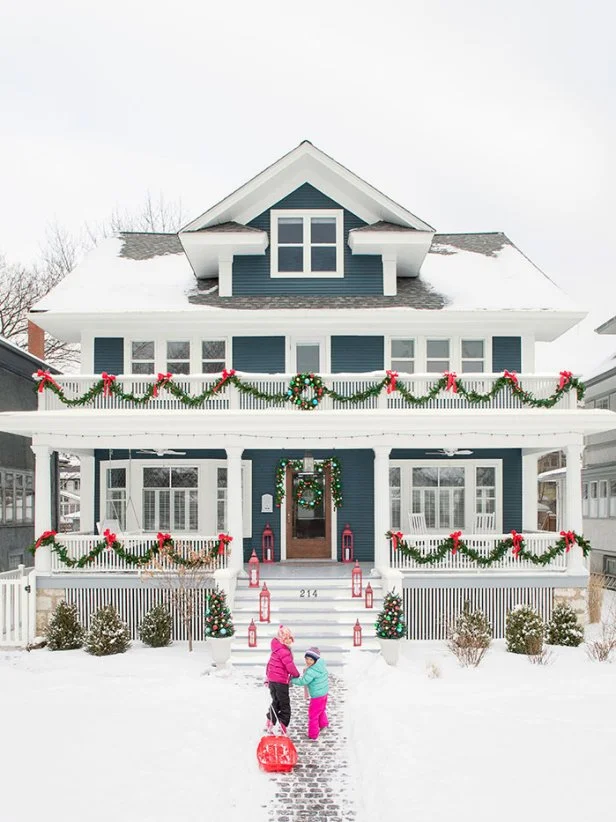 Two children walk toward a blue house adorned with Christmas wreaths and garlands, surrounded by snow and red lanterns—a moment of warmth perfect for reflection or reviewing your year-end divorce checklist. From Lawrence Law Firm New Jersey Family Lawyer.