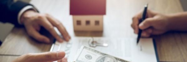 Two people sit at a table exchanging money, with a small house model, house keys, and documents being signed, suggesting a real estate transaction. From Lawrence Law Firm New Jersey Family Lawyer.