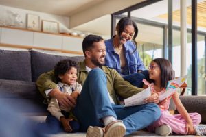 A family of four sits together in a living room, smiling and talking. The child on the right holds a drawing with a rainbow. From Lawrence Law Firm New Jersey Family Lawyer.